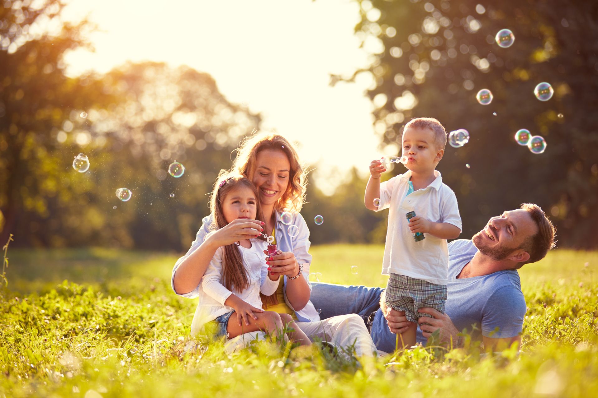 Eine vierköpfige Familie pustet Seifenblasen auf einem Feld